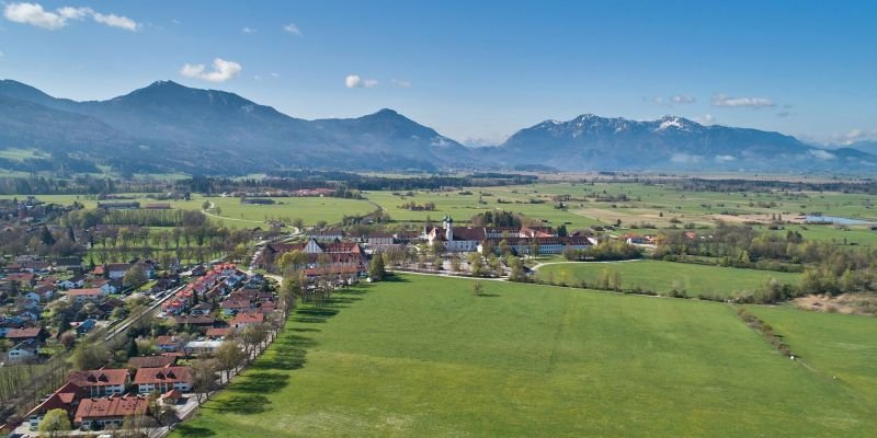 Luftaufnahme des Klosters Benedikbeuern am Ortsrand vor Bergpanorama