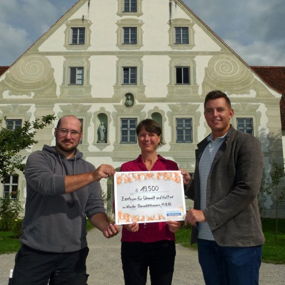 Der Scheck der Sparda Bank wird dem Leiter des ZUK Benedikt Hartmann vor dem Maierhof übergeben