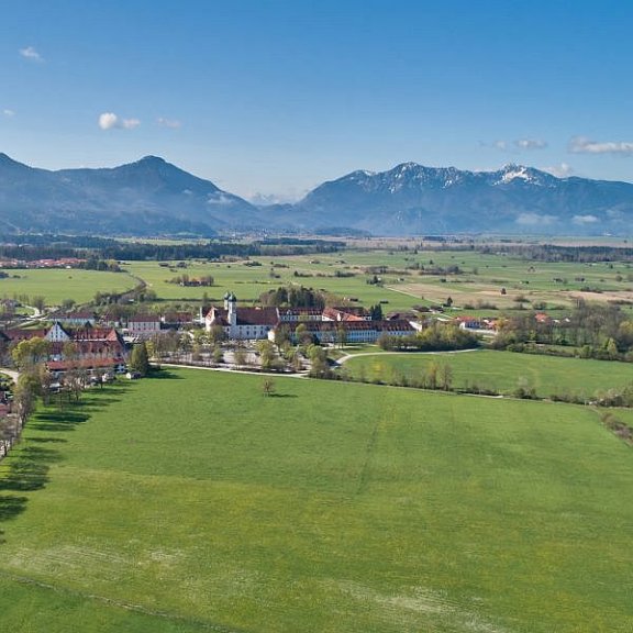 Luftaufnahme des Klosters Benedikbeuern am Ortsrand vor Bergpanorama