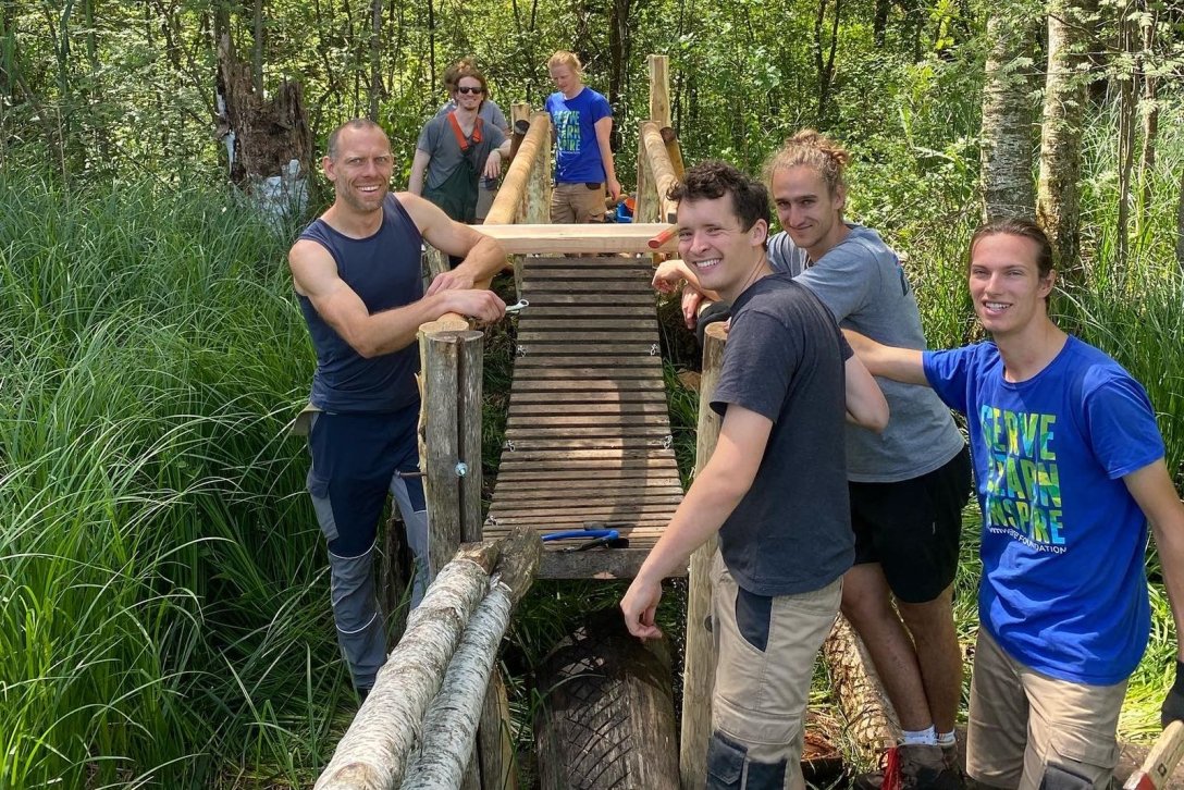 Gruppe Freiwilliger des Zentrums für Umwelt und Kultur Benediktbeuern bei der Arbeit an einer Brücke in der Moorlandschaft 